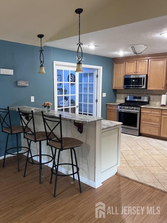 kitchen with a kitchen bar, light wood finished floors, tasteful backsplash, and appliances with stainless steel finishes