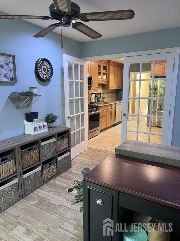 kitchen featuring light wood finished floors, glass insert cabinets, brown cabinets, appliances with stainless steel finishes, and a ceiling fan