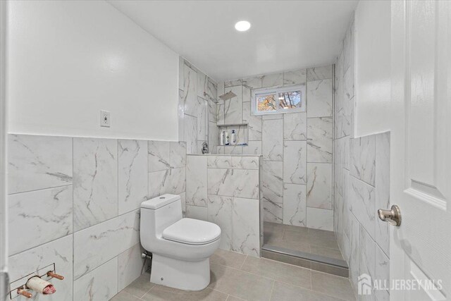 bathroom with tile patterned floors, toilet, tile walls, and a tile shower