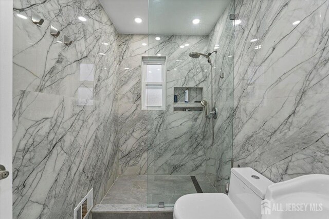 bathroom featuring tiled shower, toilet, and tile walls