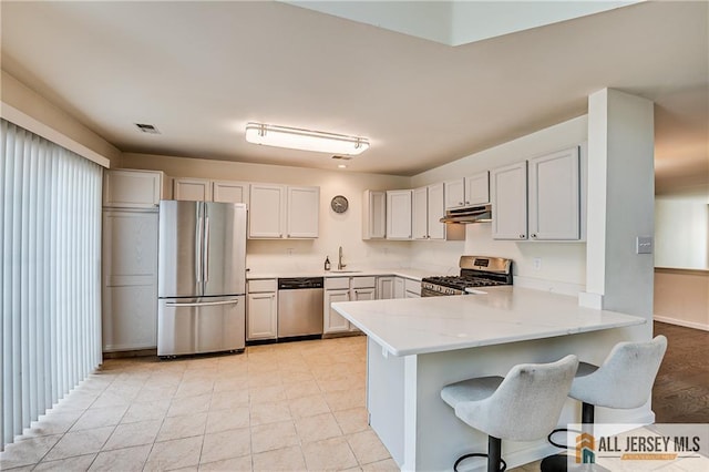 303 Harvest Ln, South Brunswick, NJ 08852 - kitchen with stainless steel appliances, a peninsula, under cabinet range hood, a kitchen bar, and light stone counters