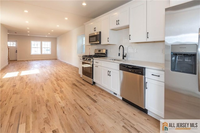 kitchen with appliances with stainless steel finishes, sink, white cabinets, light hardwood / wood-style floors, and light stone countertops