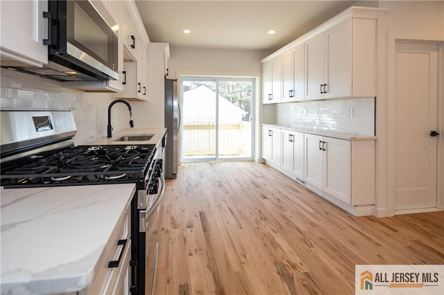 kitchen with white cabinetry, sink, light stone counters, light hardwood / wood-style floors, and stainless steel appliances