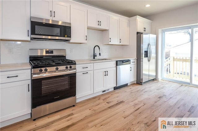 kitchen featuring appliances with stainless steel finishes, tasteful backsplash, sink, white cabinets, and light hardwood / wood-style flooring