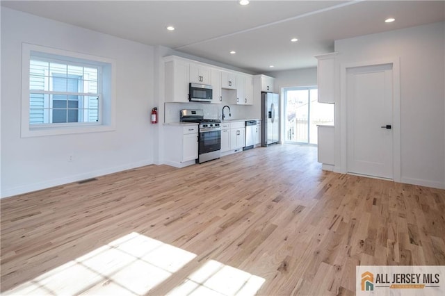 kitchen with sink, stainless steel appliances, light hardwood / wood-style floors, white cabinets, and decorative backsplash