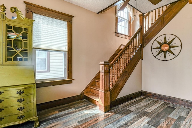 stairway with a textured ceiling, baseboards, and wood finished floors