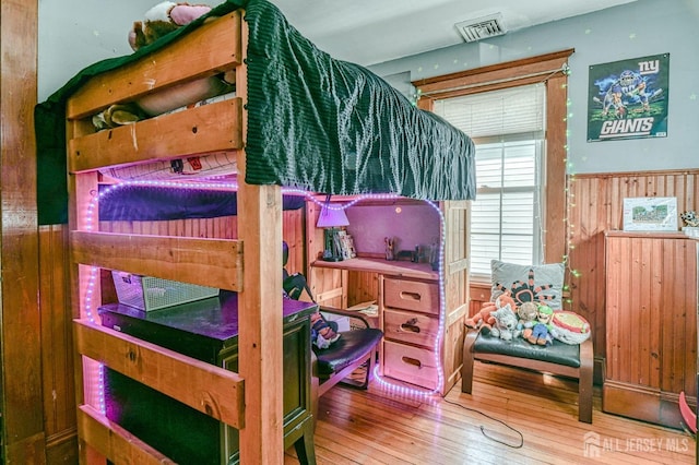 bedroom with hardwood / wood-style floors, visible vents, and wooden walls