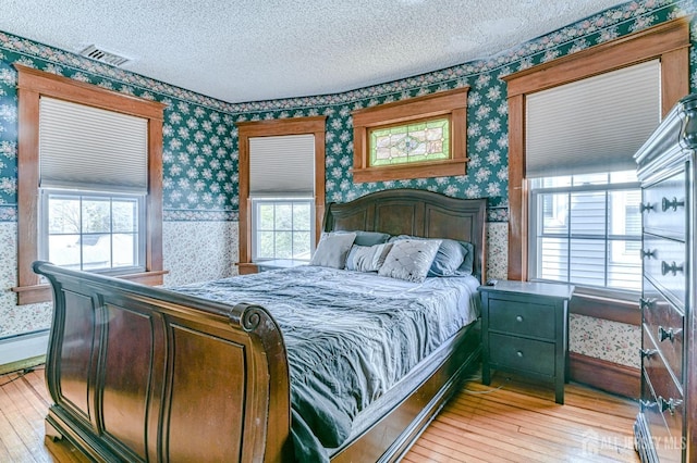 bedroom with visible vents, a textured ceiling, light wood finished floors, and wallpapered walls