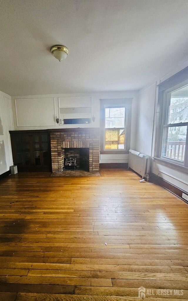 unfurnished living room with light hardwood / wood-style flooring, a brick fireplace, and radiator heating unit