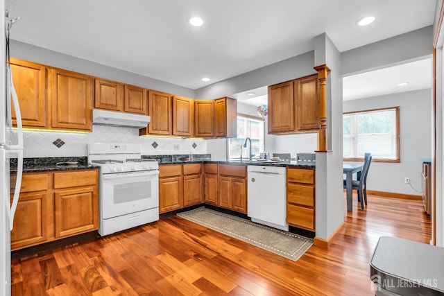 kitchen with under cabinet range hood, white appliances, dark wood-type flooring, decorative backsplash, and brown cabinetry