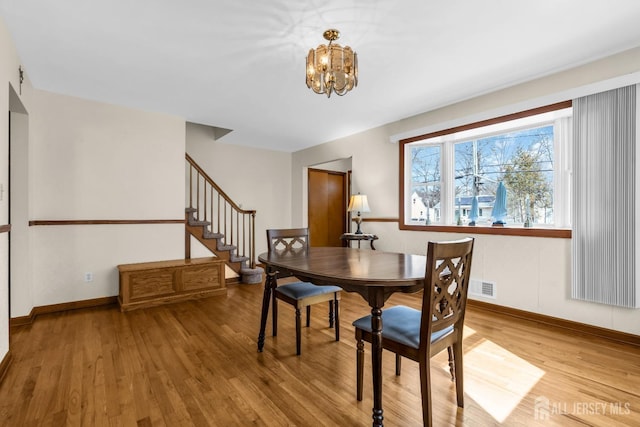 dining space with light wood finished floors, visible vents, a chandelier, baseboards, and stairs