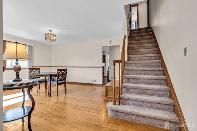 stairs with a chandelier, wood finished floors, visible vents, and baseboards