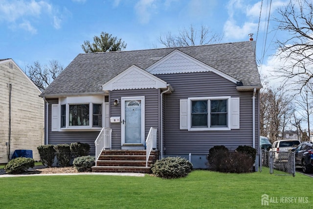 bungalow-style home with roof with shingles, fence, and a front lawn