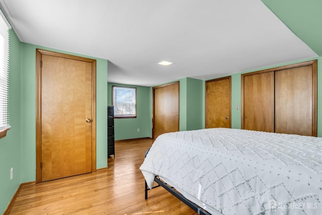 bedroom with light wood finished floors, baseboards, and two closets