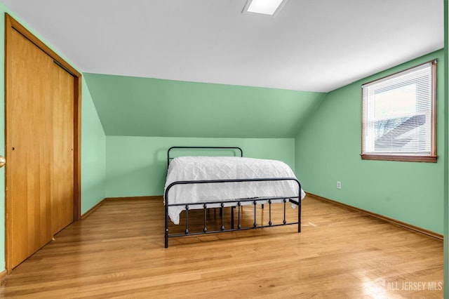 bedroom with light wood-type flooring, baseboards, vaulted ceiling, and a closet