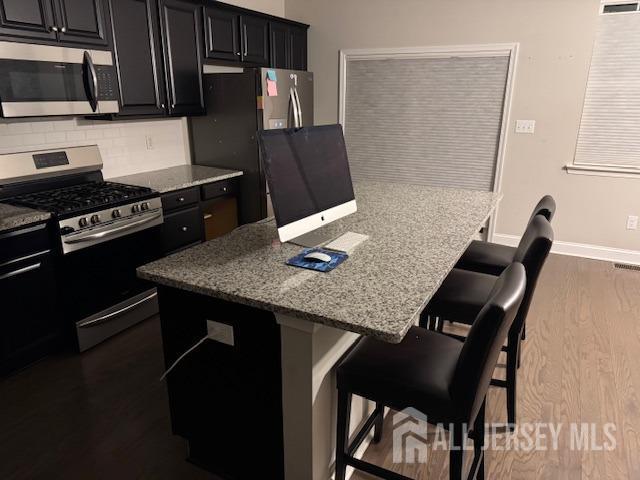 kitchen with a kitchen bar, appliances with stainless steel finishes, backsplash, light stone counters, and a kitchen island