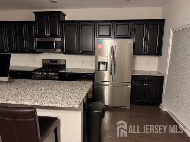 kitchen with backsplash, a kitchen bar, light stone countertops, and stainless steel appliances