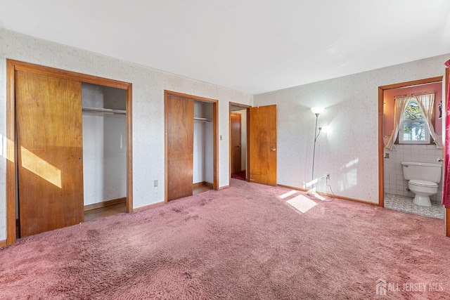 unfurnished bedroom with light carpet, ensuite bath, and multiple closets