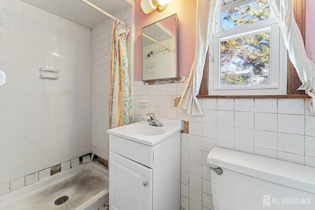 bathroom with toilet, vanity, a tile shower, and tile walls