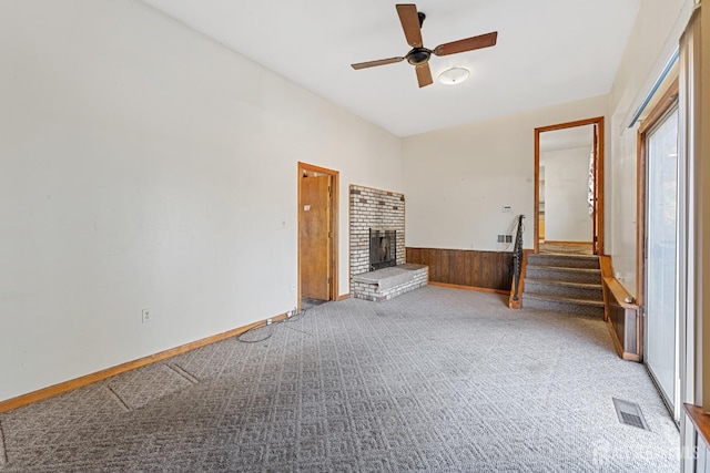 carpeted spare room featuring wooden walls, visible vents, a wainscoted wall, stairs, and a fireplace