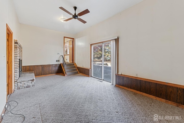 unfurnished living room with wooden walls, a wainscoted wall, stairway, carpet, and a brick fireplace