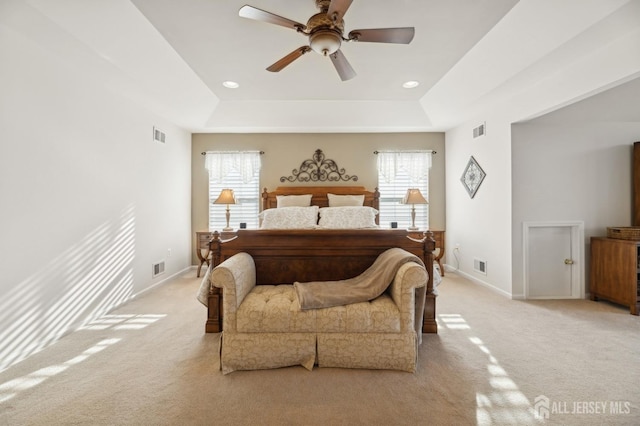 bedroom featuring a raised ceiling, light colored carpet, and ceiling fan