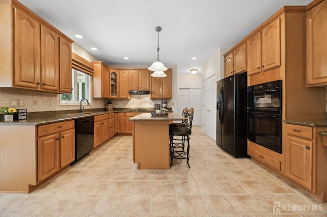 kitchen featuring dark stone countertops, a kitchen island, black appliances, a kitchen bar, and sink