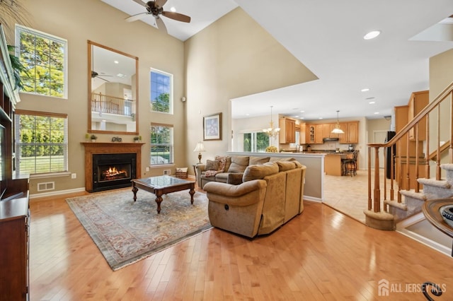 living room featuring ceiling fan with notable chandelier, a high ceiling, and light hardwood / wood-style flooring