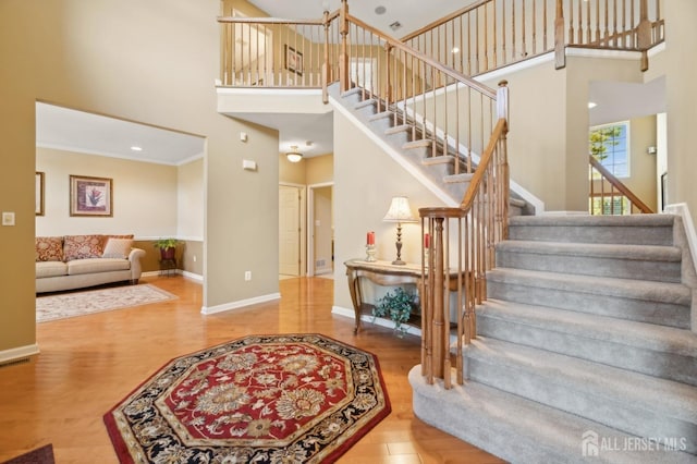 staircase featuring a high ceiling, ornamental molding, and hardwood / wood-style floors