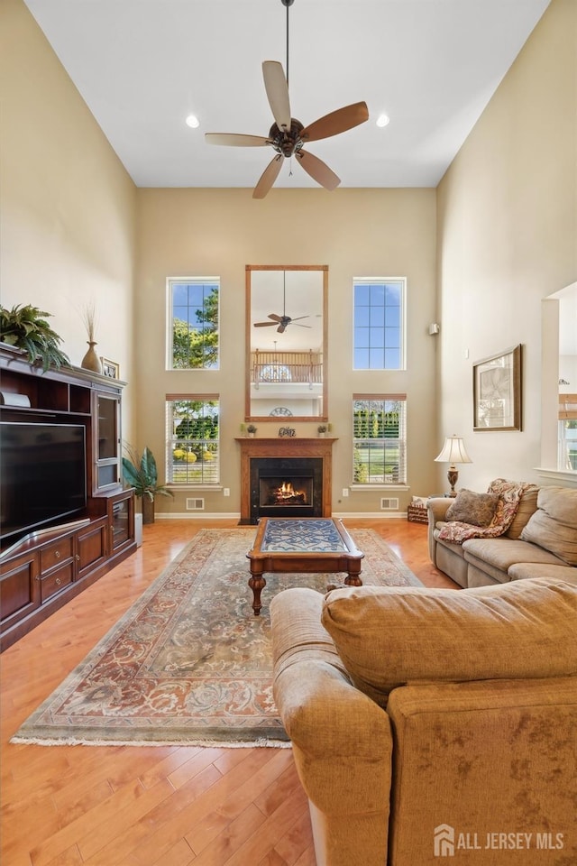 living room featuring ceiling fan, a towering ceiling, and hardwood / wood-style flooring