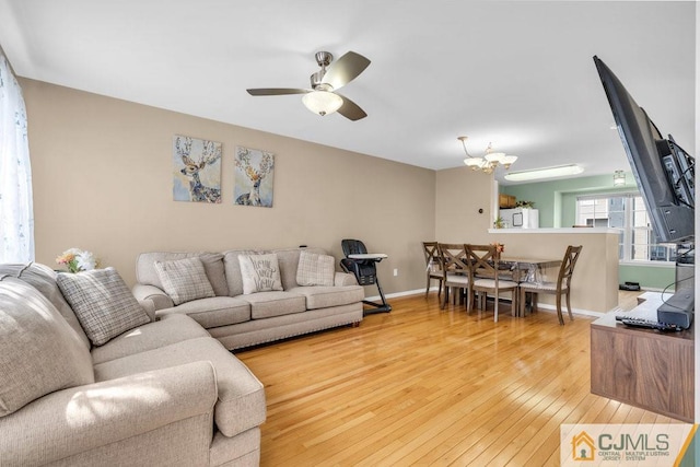 living room with ceiling fan with notable chandelier and light hardwood / wood-style floors