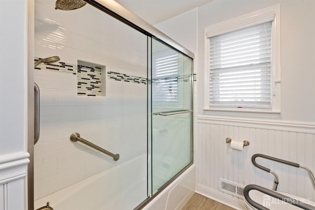 bathroom with toilet, hardwood / wood-style floors, and combined bath / shower with glass door