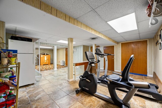 workout area with wood walls and a drop ceiling