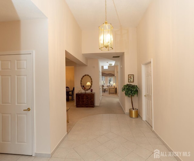 hall featuring baseboards, a high ceiling, visible vents, and a notable chandelier