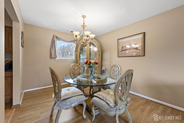 dining space with light wood-type flooring, an inviting chandelier, and baseboards