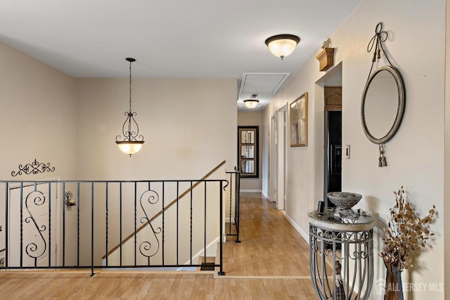 hall with an upstairs landing, baseboards, attic access, and wood finished floors