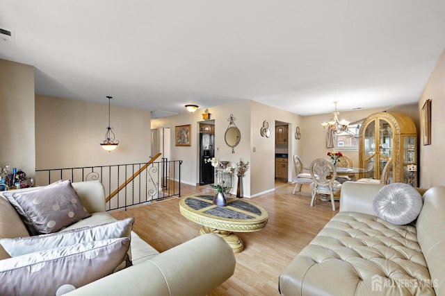 living area featuring a chandelier, wood finished floors, baseboards, and visible vents