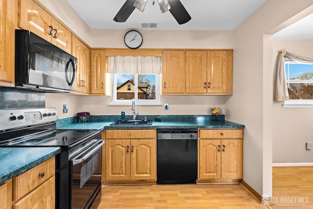 kitchen with ceiling fan, black appliances, a sink, dark countertops, and light wood finished floors