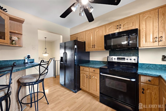 kitchen featuring light wood-style floors, ceiling fan, black appliances, dark countertops, and hanging light fixtures