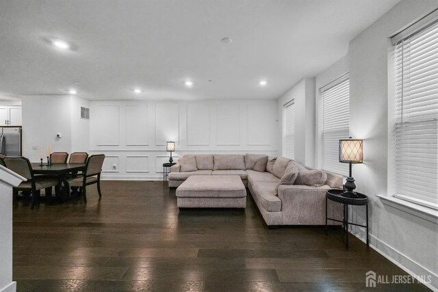 living room featuring visible vents, baseboards, recessed lighting, a decorative wall, and dark wood-style flooring