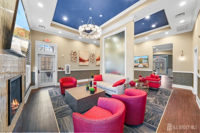 living room featuring wood finished floors, visible vents, a fireplace, crown molding, and a raised ceiling