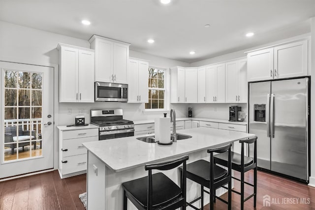 kitchen featuring a sink, dark wood-type flooring, appliances with stainless steel finishes, white cabinetry, and a kitchen island with sink