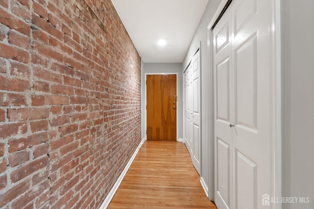 corridor with light wood finished floors and brick wall