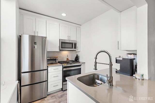 kitchen featuring a sink, white cabinets, appliances with stainless steel finishes, backsplash, and light stone countertops