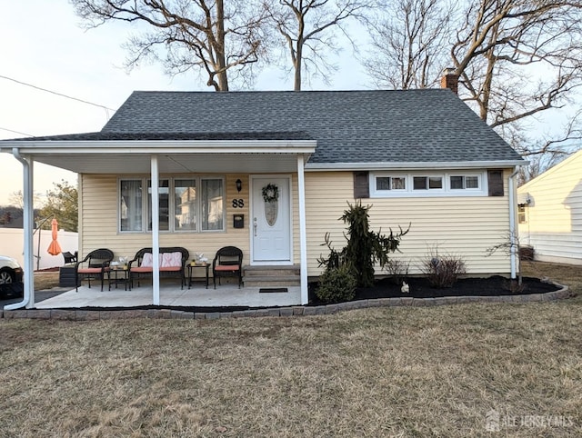 view of front facade featuring entry steps, a chimney, roof with shingles, a patio area, and a front lawn