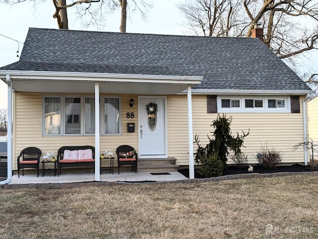 view of front of house with a front yard, entry steps, a chimney, and roof with shingles