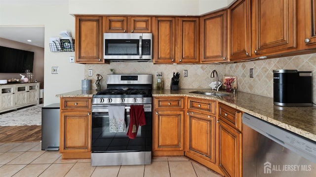 kitchen featuring stainless steel appliances, light tile patterned floors, light stone counters, decorative backsplash, and sink