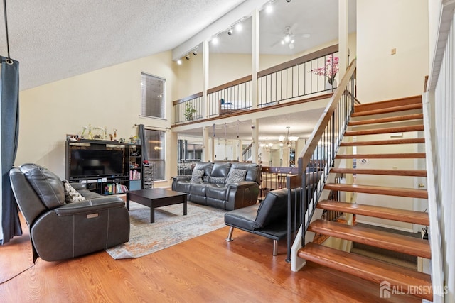 living room featuring ceiling fan with notable chandelier, high vaulted ceiling, a textured ceiling, stairway, and wood finished floors