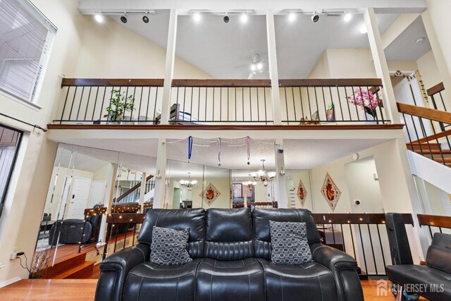 living area with ceiling fan with notable chandelier, high vaulted ceiling, rail lighting, wood finished floors, and stairs