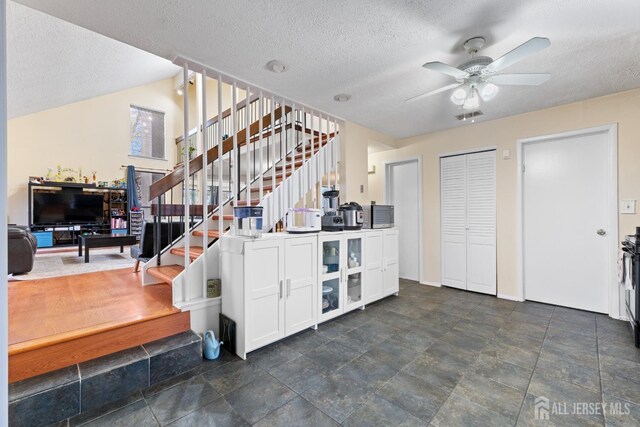 interior space featuring glass insert cabinets, a textured ceiling, white cabinetry, a ceiling fan, and visible vents